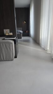 Podłoga z szarego mikrocementu Festfloor w nowoczesnej sypialni z ciemnymi ścianami i jasnymi zasłonami